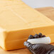 A person in gloves uses a Choice cheese wire to cut a block of cheese.