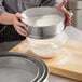 A woman uses a Choice stainless steel sieve to sift flour into a bowl.