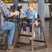 A man helping a little girl in a Lancaster Table & Seating wooden high chair.
