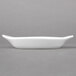 A white rectangular Hall China au gratin dish with a curved edge on a gray surface.