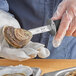 A person using a Schraf Providence Style oyster knife to open an oyster on a table.