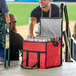 A man wearing a baseball uniform smiles while opening a red Choice insulated cooler bag filled with cans of beer.