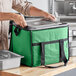 A person holding a green Choice insulated cooler bag with a metal pan inside.