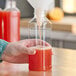 A hand pouring orange liquid into a clear square PET juice bottle.