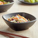 A table with two black square melamine bowls filled with salads and chopsticks.