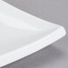 A close up of a CAC Tokyia bone white square porcelain plate with a curved edge.