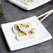 A pair of chopsticks on a CAC Tokyia white porcelain plate with sushi.