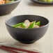 A black matte melamine bowl filled with food with a chopstick in it.