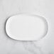 A white GET Enterprises Riverstone melamine oval plate on a marble surface.