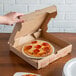 A hand reaching for a pepperoni pizza on a white 8" corrugated circle in a box.