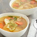 Two bowls of chicken soup with carrots and parsley on a white background.