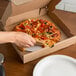 A hand slicing a pizza on a white corrugated pizza circle in a box.