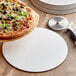 A 12" white corrugated pizza circle with a pizza on a wooden plate.
