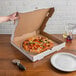 A hand holding a 14" white corrugated pizza circle in a box.