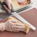 A person in gloves using a Mercer Culinary left-handed bread knife to cut a sandwich.