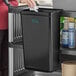 A woman using a black Choice refuse bin on a cart in a professional kitchen.