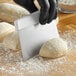 A person in black gloves using a Choice stainless steel dough cutter to cut white floured dough.