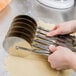 A person using an Ateco stainless steel wheel pastry cutter to cut dough.