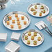 A stack of Acopa stainless steel catering platters on a table with white plates and a glass.