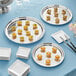 A group of Acopa stainless steel platters and white plates with food on them.