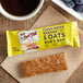 A Bob's Red Mill Peanut Butter Banana & Oats bar on a table with a cup of coffee.