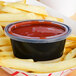 A clear oval plastic souffle cup lid on a container of ketchup on french fries.