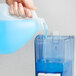 A hand pouring Dial Spring Water liquid hand soap into a blue plastic container.