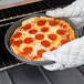 A person in white gloves holding a pizza in a Chicago Metallic deep dish pizza pan.