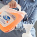 A person pouring orange Dial Complete foaming hand soap into a jug.