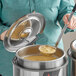 A woman using a Jacob's Pride ladle to serve soup from a Vollrath stainless steel pot.