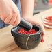 A person grinding red pepper with a black Fox Run mortar and pestle.