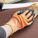 A hand wearing a Mercer Culinary orange and white food processing glove cutting bread.