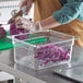 A person wearing gloves uses a knife to cut purple cabbage into a plastic container.