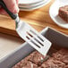 A hand using an OXO mini turner to serve a brownie in a pan.