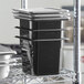 A stack of Vigor black food pans and lids on a metal rack.
