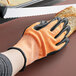 A hand wearing an orange and white Mercer Culinary Millennia cut-resistant glove cutting bread.