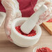 A person in gloves using a Fox Run white marble mortar and pestle to crush red berries.