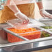 A person in gloves using a Vigor clear plastic food pan to serve food at a salad bar.
