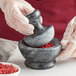 A person in gloves using a Fox Run black marble mortar and pestle to grind red pepper.