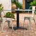 A table with a Lancaster Table & Seating Excalibur black table base on a brick patio with two chairs.