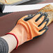 A hand wearing a small orange and white Mercer Culinary Millennia Cut-Resistant glove cutting a piece of bread.