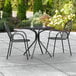 A Lancaster Table & Seating Harbor outdoor patio table with black chairs on a patio.