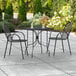 A Lancaster Table & Seating Harbor black rectangular outdoor table with ornate legs and two chairs on a patio.