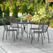A Lancaster Table & Seating Harbor black square table with ornate legs and two black chairs on a patio.