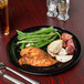 A Carlisle black melamine plate with chicken, potatoes, and green beans on a table.