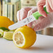 A person using a green Mercer Culinary paring knife to cut a lemon on a counter.
