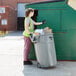 A woman in a safety vest putting garbage into a Rubbermaid 44 gallon gray trash can.
