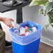 A hand pours water from a plastic bottle into a blue trash can lined with a Lavex clear plastic bag.