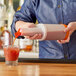 A person using a Choice plastic pour bottle with an orange spout to pour a red drink into a glass.