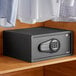 A black steel 360 Office Furniture hotel safe with electronic keypad lock on a wooden shelf.
